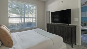 A bedroom with a bed, a TV, a dresser, and a window with blinds. - Landing | Incredible 1BD, Clubhouse (League City)