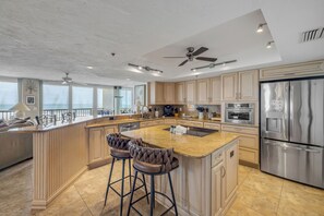 Une cuisine spacieuse dotée d’un grand îlot central, d’appareils électroménagers en acier inoxydable et d’un ventilateur de plafond.