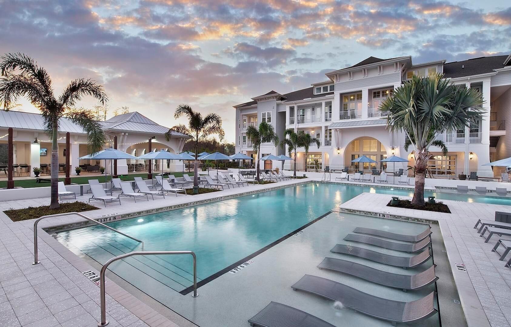 A swimming pool with lounge chairs, palm trees, and a building with balconies.