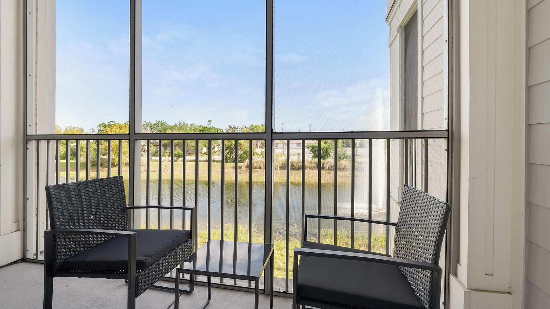Un balcon avec deux fauteuils en osier et une petite table, donnant sur une étendue d’eau et une zone verdoyante.