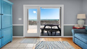 Une pièce avec une porte-fenêtre coulissante donnant sur un balcon, un canapé bleu, une petite table avec une lampe et un meuble bleu.