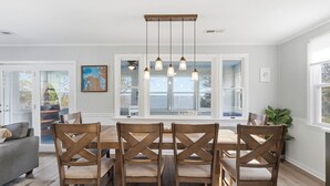 A dining area with a wooden table and chairs, a pendant light fixture, and large windows.