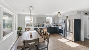 A modern kitchen with a wooden dining table, built-in appliances, and large windows.