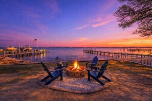 A waterfront outdoor seating area with a fire pit and Adirondack chairs. - Relax on the Sunset Sound-Hot Tub Soaks & Fire Pit Nights in Kill Devil Hills (Kill Devil Hills)