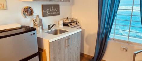 Een keuken met een koelkast, gootsteen en fornuis. Er is een raam met uitzicht op de oceaan.
