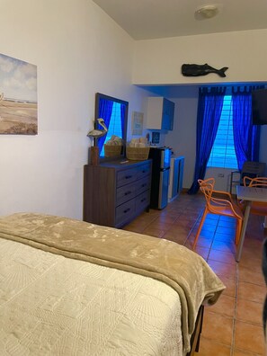 Een kamer met een bed, een bureau, een stoel, een kast en een raam met blauwe gordijnen.