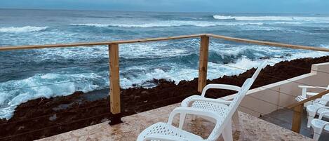 A terrace with white plastic chairs overlooking the ocean.