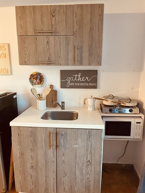 A compact kitchen with wooden cabinets, a white countertop, a sink, a stove, and a microwave.