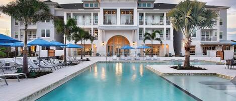 A hotel with a large pool, sun loungers, and umbrellas.