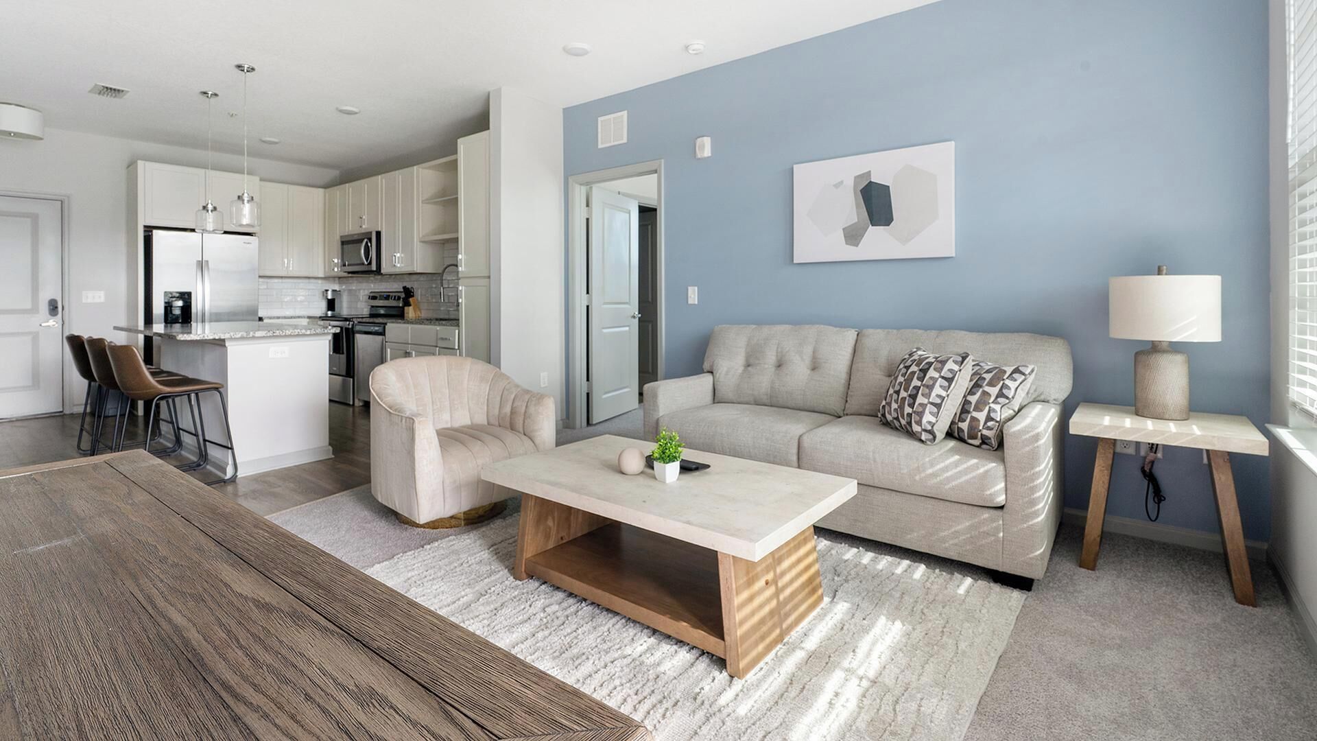 Ein modernes Wohnzimmer mit einer Couch, einem Couchtisch und einem Essbereich mit Stühlen sowie einer Küche im Hintergrund.