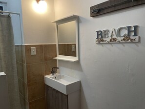 Un bagno con un lavandino bianco, uno specchio e un cartello appeso al muro con la scritta 'BEACH'.