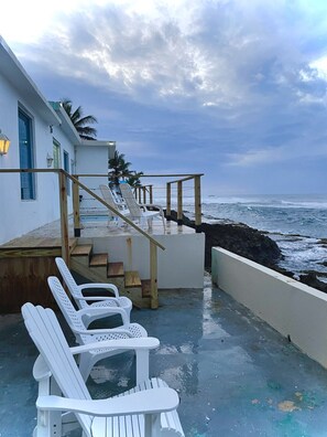 A coastal property with a wooden staircase leading to a deck with white plastic chairs.