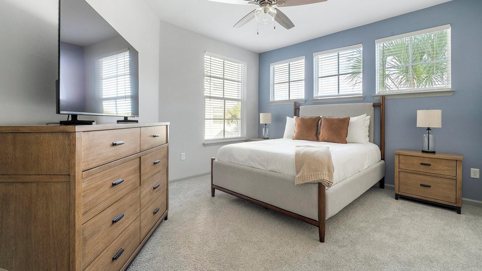 Une chambre à coucher avec un lit, une commode en bois, des tables de chevet et un ventilateur de plafond.