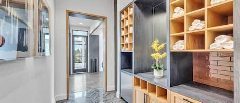 Un couloir au design moderne, une étagère en bois avec des serviettes et une plante en pot.