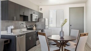 A modern kitchen with dark cabinets, stainless steel appliances, and a dining area with a round table and chairs. - Landing | Modern 2BD, Gym, Yoga Studio (Glendale)