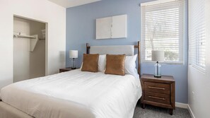 A bedroom with a bed, two nightstands, a window with blinds, a door, and a wall-mounted artwork. - Landing | Chic 2BD, Pool, Gym (Glendale)