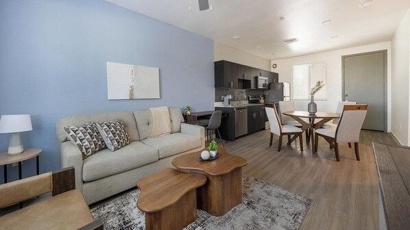 A modern living room with a sofa, coffee table, and dining area. - Landing | Chic 2BD, Pool, Gym (Glendale)
