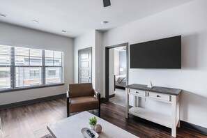 A modern hotel room with a large window, a desk, a chair, and a flat-screen TV. - Landing | Beautiful 2BD, Clubhouse, Gym (Louisville)