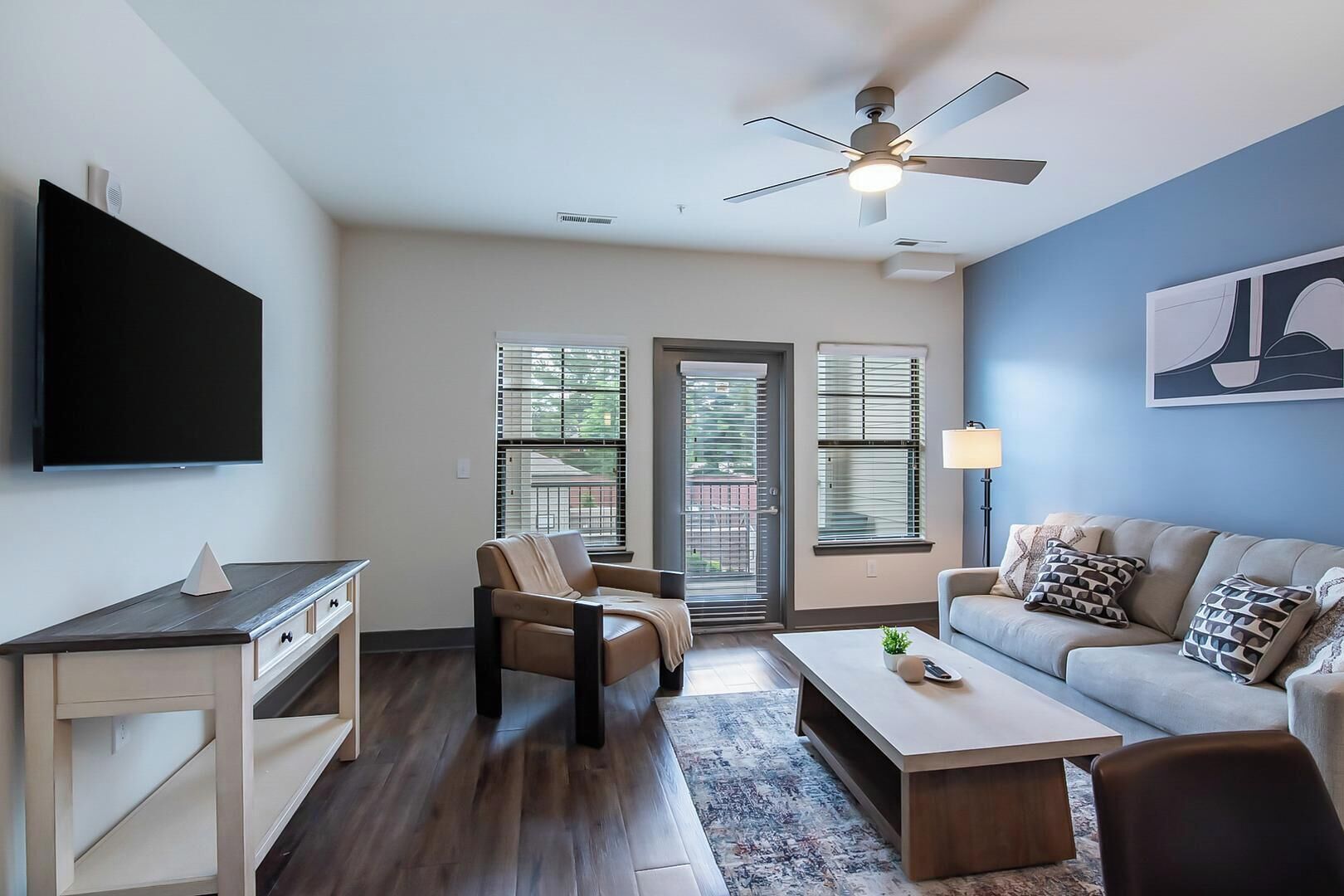 A living room with a flat-screen TV, a ceiling fan, a sofa, a coffee table, and a chair.