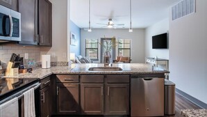 Une cuisine moderne avec des meubles de couleur sombre, un plan de travail en granit, un four à micro-ondes encastré et un ventilateur de plafond.