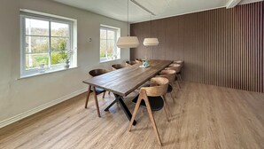 Ein Konferenzraum mit einem langen Holztisch, mehreren Stühlen, großen Fenstern und einer Wand mit Lamellen.