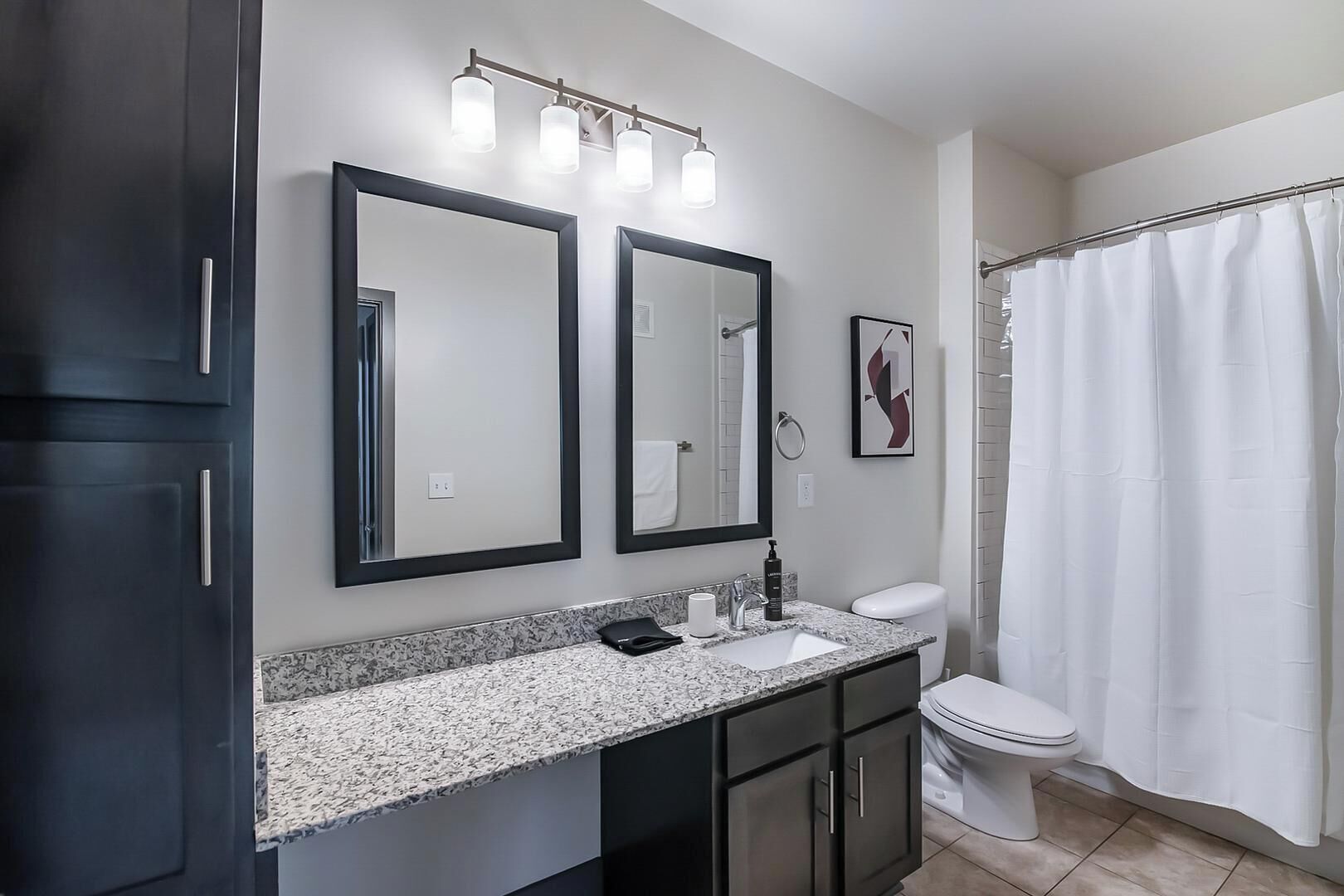 Un baño con lavabo doble, dos espejos, inodoro y cortina de ducha.