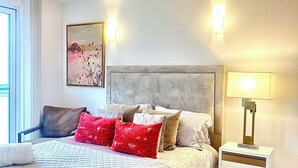 A bedroom with a bed, pillows, a nightstand, a lamp, a chair, and a painting on the wall. - Luxury apartment in Canary Wharf (London)