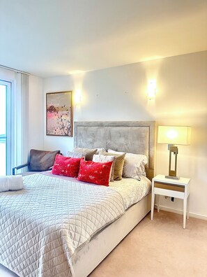 A bedroom with a bed, pillows, a nightstand, a lamp, a chair, and a painting on the wall. - Luxury apartment in Canary Wharf (London)