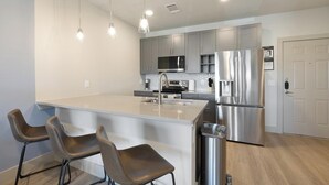 A modern kitchen with a central island, stainless steel appliances, and bar stools. - Landing | Spectacular 1BD, Clubhouse, Game Room (Mansfield)