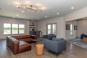 Ein modernes Wohnzimmer mit Ledersofas, einem Couchtisch und einem grauen Sessel. Es gibt eine Küchenzeile mit Spüle und Schränken sowie einen Balkon mit Geländer.