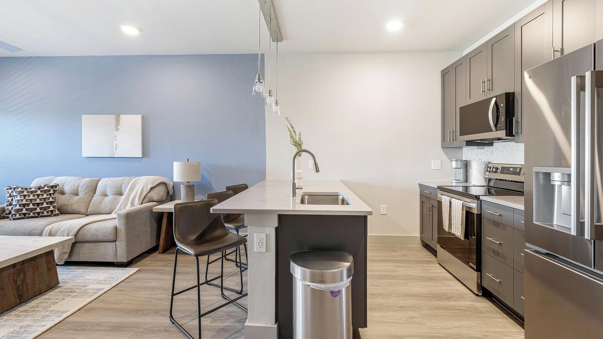 Una cocina moderna con electrodomésticos de acero inoxidable, una barra y una zona de estar con sofá y sillones.