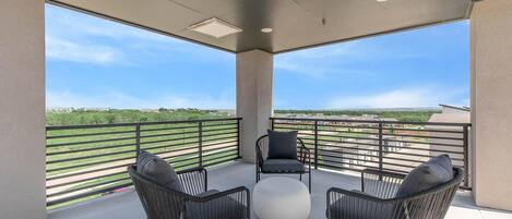 A balcony with two wicker chairs, a round white table, and a view of a green landscape.