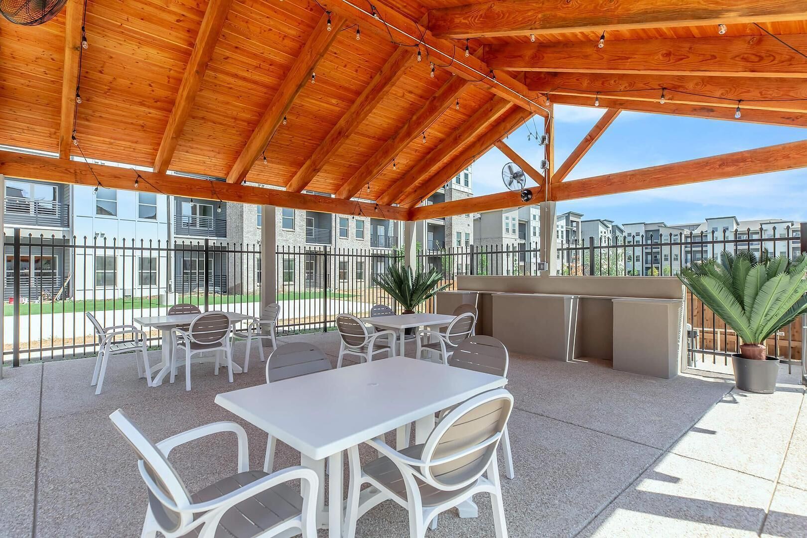 An outdoor patio with tables and chairs, a fan, and a potted plant.