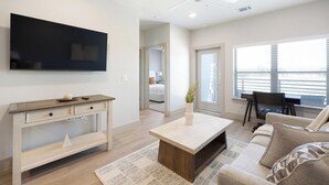 En moderne stue med et fladskærms-TV, et træskrivebord, en sofa og et spiseområde.