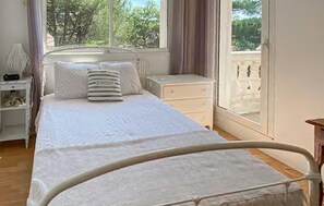 A bedroom with a bed, a nightstand, a dresser, and a window with a view of trees.