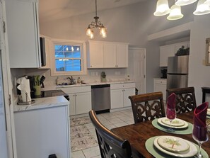 A kitchen with white cabinets, a stainless steel refrigerator, a dining table with chairs, and a chandelier.