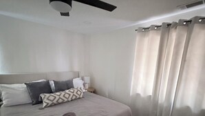 Ein Schlafzimmer mit einem Bett, Kissen, einer Decke, einem Deckenventilator und Vorhängen.