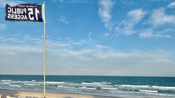Une plage avec un drapeau, une promenade en bois et des vagues de l’océan.
