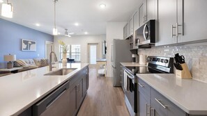 Uma cozinha moderna com eletrodomésticos de aço inoxidável, uma ilha central e vista para a sala de estar.