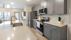 A modern kitchen with grey cabinets, stainless steel appliances, a large island with a sink, and a microwave above the stove. - Landing | Beautiful 2BD, Clubhouse, Game Room (Mansfield)