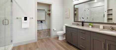 A modern bathroom with a glass shower enclosure, a toilet, a sink with a mirror, and a wooden floor.