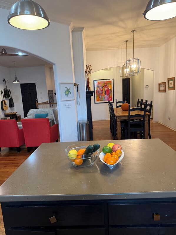 Un îlot de cuisine avec des corbeilles de fruits, un coin repas avec des chaises, un canapé rouge et un mur décoré de guitares.