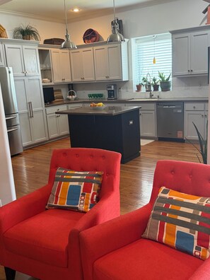 Une cuisine moderne avec des meubles blancs, un îlot central noir et des chaises rouges dotées de coussins à motifs.
