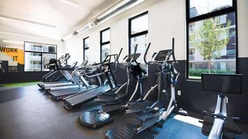 A gym with treadmills, stationary bikes, and a large window with a view of buildings.