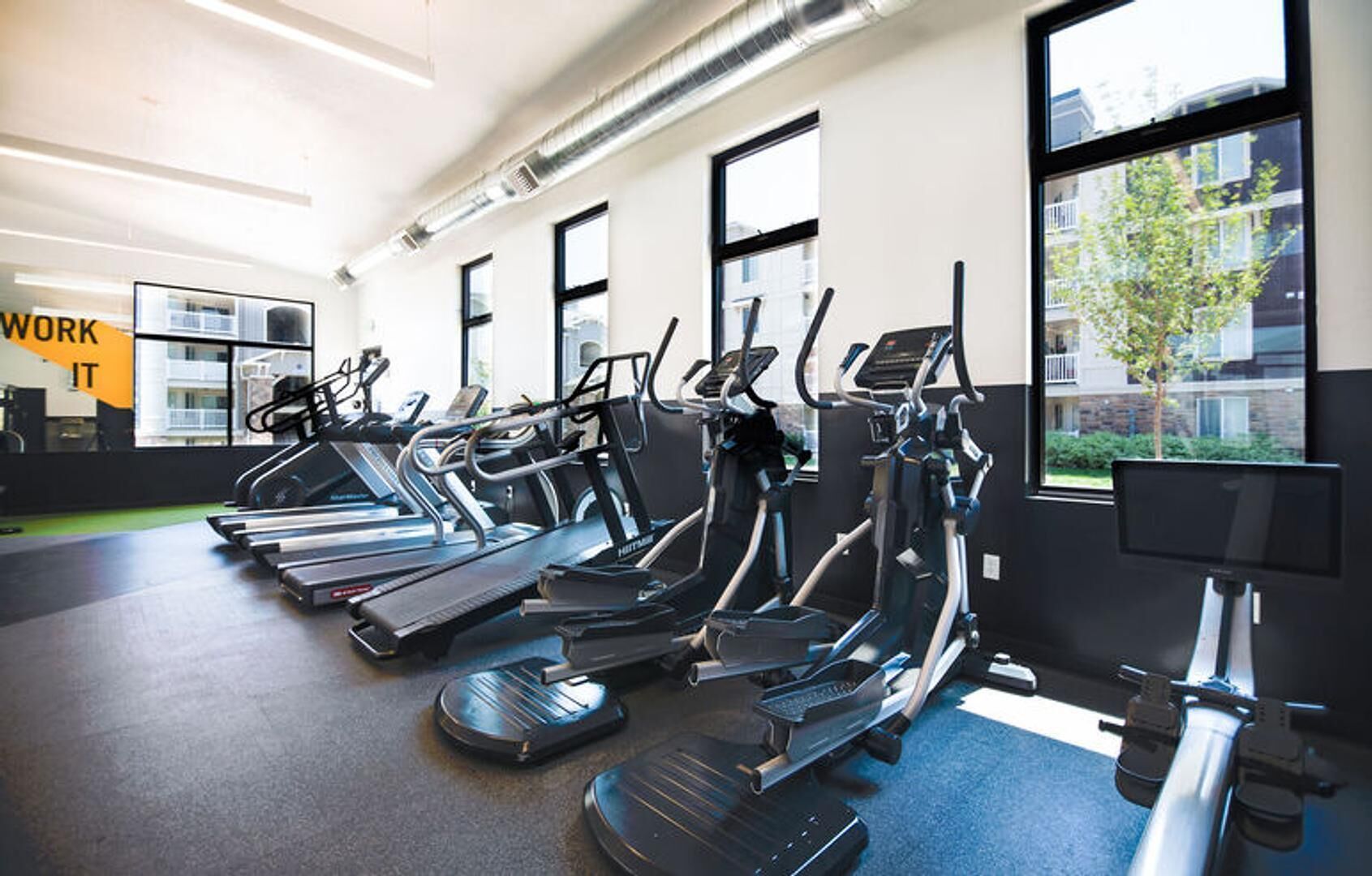 A gym with treadmills, stationary bikes, and a large window with a view of buildings.