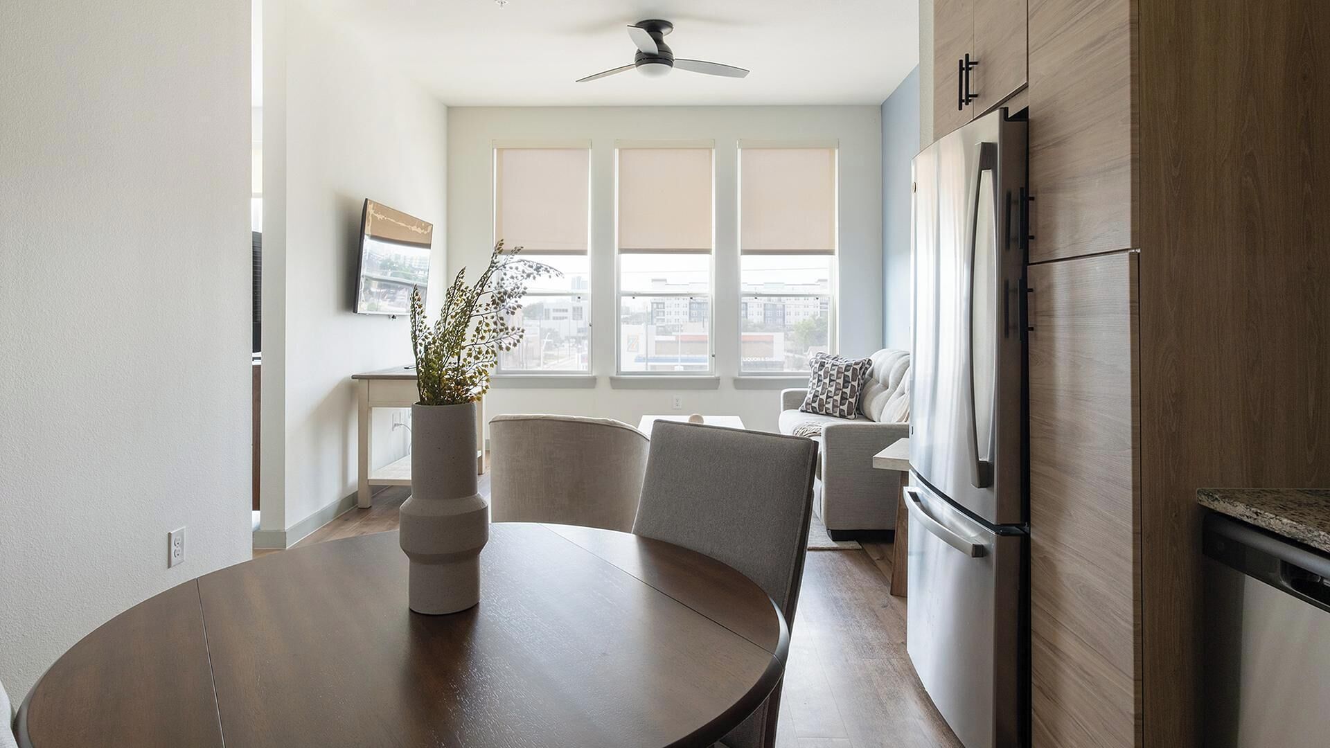 A modern kitchen with a dining table, chairs, a refrigerator, and a ceiling fan.