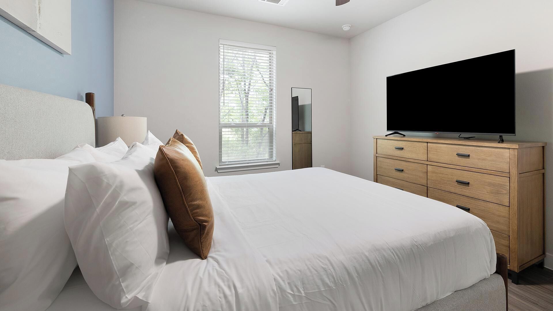 Ein Schlafzimmer mit Bett, Fernseher, Kommode und einem Fenster mit Jalousien.