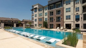 Un edificio residenziale a più piani con piscina, sdraio e una zona patio coperta.