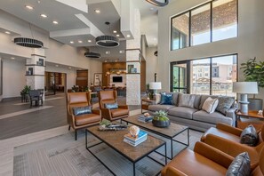 Eine großzügige Lobby mit Ledersesseln, einer Couch und einem Couchtisch. Es gibt Pendelleuchten, einen Kamin und große Fenster mit Blick ins Freie.