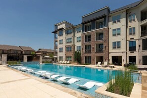 Ein mehrgeschossiges Wohnhaus mit Pool, Liegestühlen und einer überdachten Terrasse.